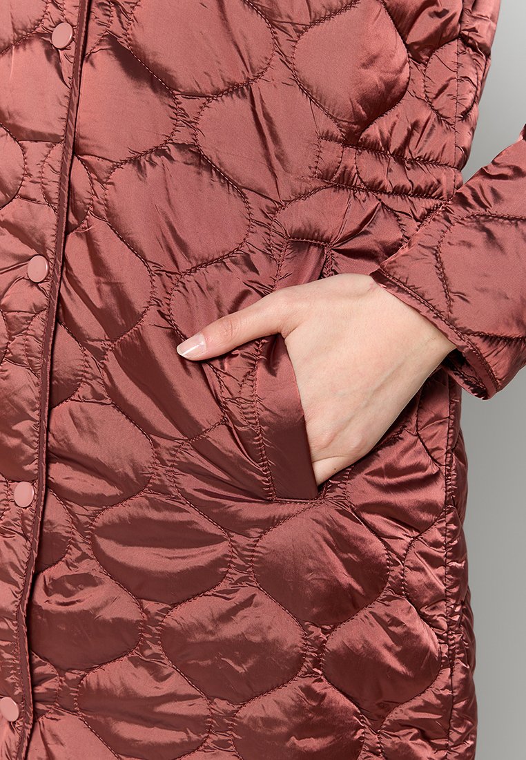 Gevoerde pufferjas in roestbruin, met een gladde, glanzende textuur, ronde patronen en zijzakken met knoopsluiting.