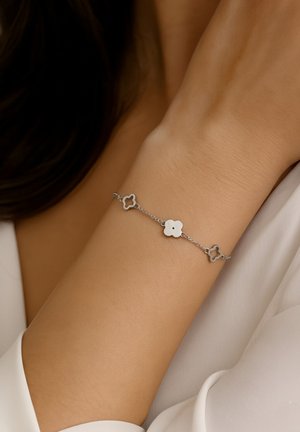 Bracciale a catena d'argento con tre maglie a forma di fiore, alternando un centro bianco solido e un design a traforo metallico.