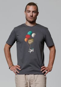 Graues Baumwoll-T-Shirt mit einer Astronautenillustration, der bunte, planetenförmige Ballons hält. Kurze Ärmel und ein klassisches Rundhalsdesign.