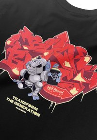 Zwarte katoenen t-shirt met een kleurrafie graffiti-achtige illustratie. Illustraties bevatten een cartoongorilla en de tekst "Transform the Generation" in vetgedrukte letters.
