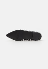 Semelle plate pointue noire de chaussure tournée vers le haut, décorée de clous argentés espacés uniformément tout autour des bords.