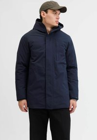 Marineblaue isolierte Jacke mit Kapuze, ausgestattet mit einem frontalen Reißverschluss und seitlichen Reißverschlusstaschen. Glatte Textur und modernes Design.