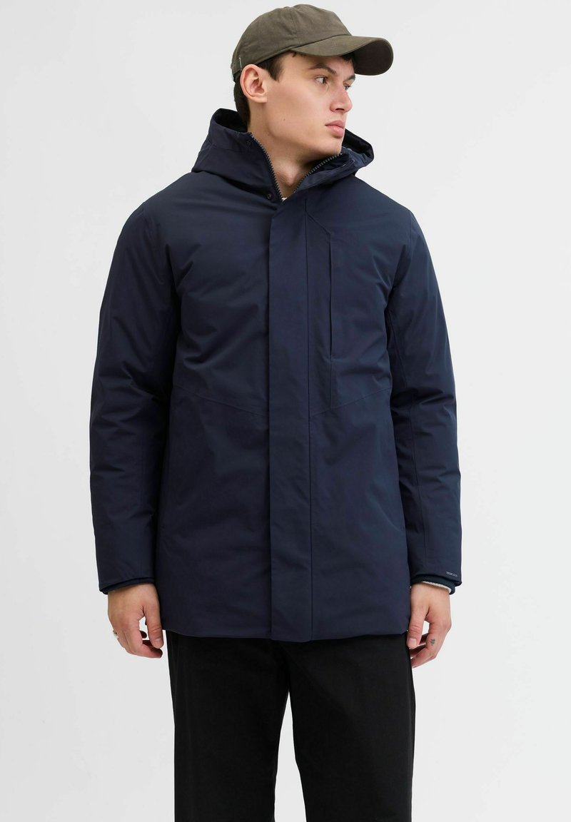 Marineblaue isolierte Jacke mit Kapuze, ausgestattet mit einem frontalen Reißverschluss und seitlichen Reißverschlusstaschen. Glatte Textur und modernes Design.