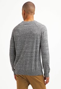 Szary sweter o fakturze z okrągłym dekoltem i długimi rękawami. Posiada ściągacze przy dole i mankietach. Noszony z beżowymi spodniami, prezentuje swobodny fason.