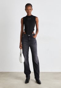 Bodies negro sin mangas con recortes, combinado con jeans de mezclilla oscuros y un bolso blanco. Diseño minimalista con líneas y texturas limpias.