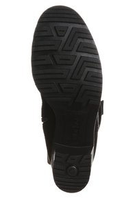 Semelle de chaussure en caoutchouc noir avec des motifs de grip texturés, présentant une forme arrondie et un talon plat. Comprend un logo circulaire et des bords renforcés.