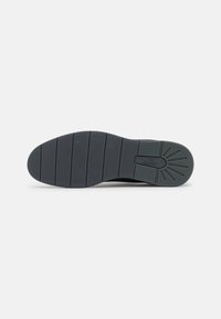 Semelle d'une chaussure de couleur sombre avec des lignes d'adhérence à motif et une section rectangulaire de marque près du talon.