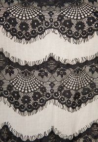 Zwarte kanten stof met ingewikkelde bloempatronen, gegolfde randen en franjes tegen een lichte achtergrond.