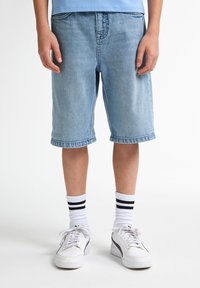 Shorts en denim bleu clair à coupe décontractée, avec des ourlets retroussés, associés à des baskets blanches et des chaussettes à rayures noires.