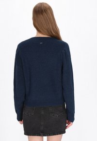 Marineblauwe gebreide trui met een geribbelde textuur, ronde halslijn en verlaagde schoudernaad, gecombineerd met een zwarte denimrok.