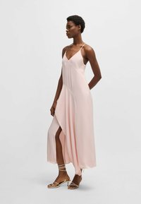 Jasnoróżowa satynowa sukienka z dekoltem w kształcie litery V i cienkimi ramiączkami, z asymetrycznym dołem i bocznym rozcięciem. Uzupełniona o sandały na cienkich obCasach.