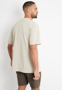 Beige bomulds t-shirt med korte ærmer, lige snit og en afslappet pasform. Kombineret med mørk olivengrønne shorts, hvilket viser en afslappet stil.