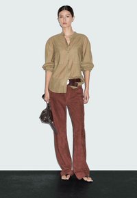 Khaki knoopshirt, roestkleurige suède broeken en een kleine zwarte handtas. Het model draagt open schoenen en een contrasterende riem.