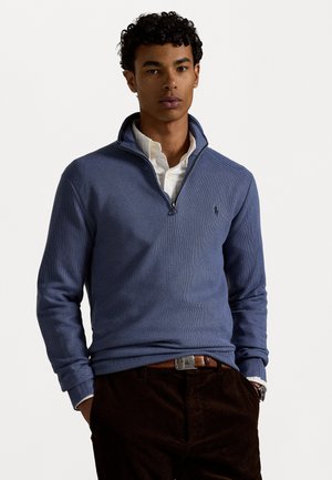 Blauwe zip-up trui met een gestructureerd patroon, gecombineerd met een witte overhemd met kraag. Bevat een klein logo op de borst en geribbelde manchetten.