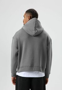 Grijze capuchontrui gemaakt van zacht materiaal, met een ontspannen pasvorm, geribbelde manchetten en zoom, en een kangaroezak.