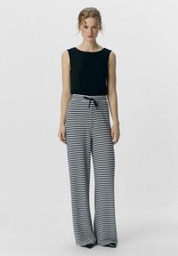 Top nero senza maniche con texture a coste abbinato a pantaloni a vita alta e gamba larga a righe navy e bianche. Chiusura con coulisse in vita.