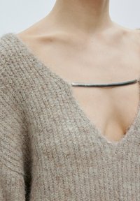 Beige gestrickter Pullover mit tiefem V-Ausschnitt und weiten Ärmeln, mit einem silbernen Reißverschlussdetail am Ausschnitt. Weiche Textur.
