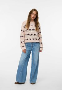 Suéter de punto en rosa claro con patrones de coronas multicolores; combinado con jeans ligeros de pierna ancha en azul y zapatos marrones. Mangas largas, tejido texturizado.