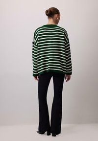 Green and white striped knit sweater with loose fit, long sleeves, and round neckline, paired with black flared pants and heeled shoes.