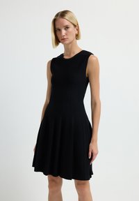 Abito nero senza maniche con corsetto aderente e gonna svasata. Presenta dettagli a righe verticali e una superficie liscia.