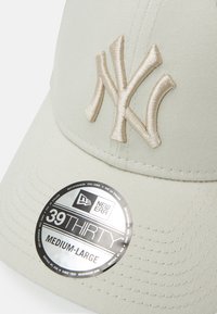Casquette beige avec logo NY en cream brodé et un tissu texturé. Elle possède une visière courbée et une étiquette New Era noire indiquant la taille.