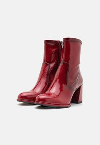 Bottines en cuir verni rouge avec un talon épais, fermeture éclair et texture lisse. Dotées d'une forme de bout allongée et d'un design élégant.