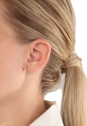 Ohrringe in Schmetterlingsform aus goldfarbenem Metall mit Ausschnitten. Leichtes Design, das am Ohrläppchen befestigt ist und einen schlanken, modernen Stil präsentiert.