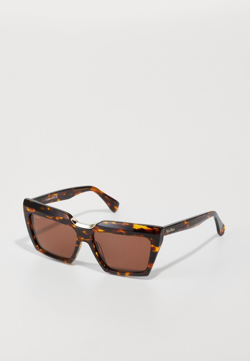 Lunettes de soleil écaille de tortue avec des montures carrées et des verres marron. Présentent un accent doré au centre et des branches solides avec un détail de marque.
