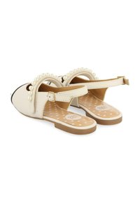 Sandalias blancas con un acabado de imitación de cuero suave, que presentan un acento de perla a lo largo de la tira y una hebilla ajustable en el tobillo. Suela plana.