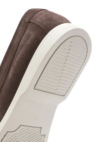 Bruine suède schoen met een witte, gestructureerde rubberen zool. De zool heeft horizontale groeven voor grip. Stiksels zijn zichtbaar langs de randen.
