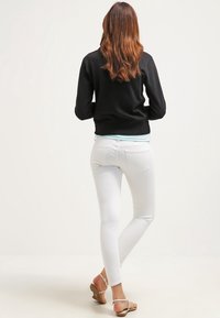 Vita smala jeans i kombination med en svart sweatshirt, som har en avslappnad passform och slät tyg. Bakifrån visas en strömlinjeformad siluett och minimal detaljering.