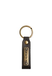 Llavero de cuero con una correa negra y una placa rectangular con acabado en bronce grabada con "SCALPERS", unida a un anillo metálico.