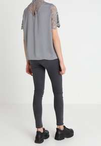 Top gris de manga corta con detalles de encaje, con abertura en la espalda en forma de ojo de cerradura, combinado con jeans skinny gris oscuro y zapatillas gruesas negras.