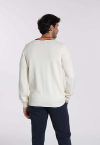 Pull en tricot blanc à manches longues et ourlet côtelé, avec un col à rayures contrastantes. Porté avec un pantalon marine.
