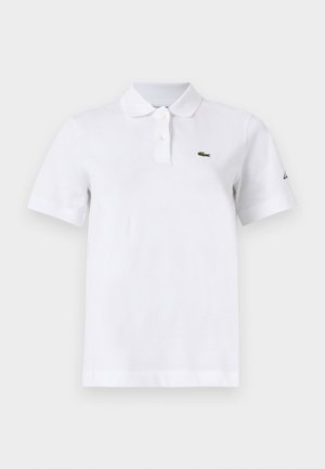 Bijela polo majica kratkih rukava s dva gumba, malim zelenim logom krokodila na lijevoj strani prsa i diskretnim crnim logom na lijevom rukavu.