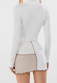 Bílý vroubkovaný rolák spárovaný s mini sukní se patchworkovým vzorem v bílé a béžové barvě, s vroubkovanými okraji a výraznými texturami.