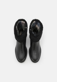 Czarne skórzane buty z puszystym czarnym kołnierzem, wewnętrzną podszewką w kratkę i bocznymi zamkami błyskawicznymi dla łatwego zakładania. Płaskie podeszwy zapewniają stabilność.