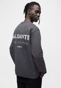Γκρι φούτερ με μεγάλο λευκό κείμενο "ALLSAINTS" και ιαπωνικούς χαρακτήρες στην πλάτη. Κλασικός σχεδιασμός με στρογγυλή λαιμόκοψη και άνετη εφαρμογή.