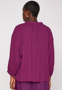 Camicia a maniche lunghe a righe viola con vestibilità ampia e colletto rilassato. Tessuto testurizzato con linee verticali visibili e polsini con bottoni.