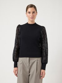Black knitted sweater with sheer black floral-patterned sleeves and ribbed cuffs. Paired with light gray pleated trousers.