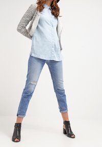 Ljust blå skjorta med knappar i kombination med slitna ljusblå jeans. En texturerad grå kavaj kompletterar svarta öppna tå ankle boots.