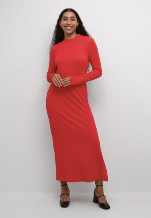 Punainen, pitkähihainen neulemaksimekko, jossa on korkea kaulus. Sujuva pinta ja muotoiltu siluetti ulottuvat nilkkapituisiksi. Esitelty mustien korkokenkien kanssa.