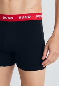 Schwarze Boxershorts mit rohem elastischen Bund, der "HUGO" in weißer Schrift zeigt. Weicher, dehnbarer Stoff mit tailliertem Design.
