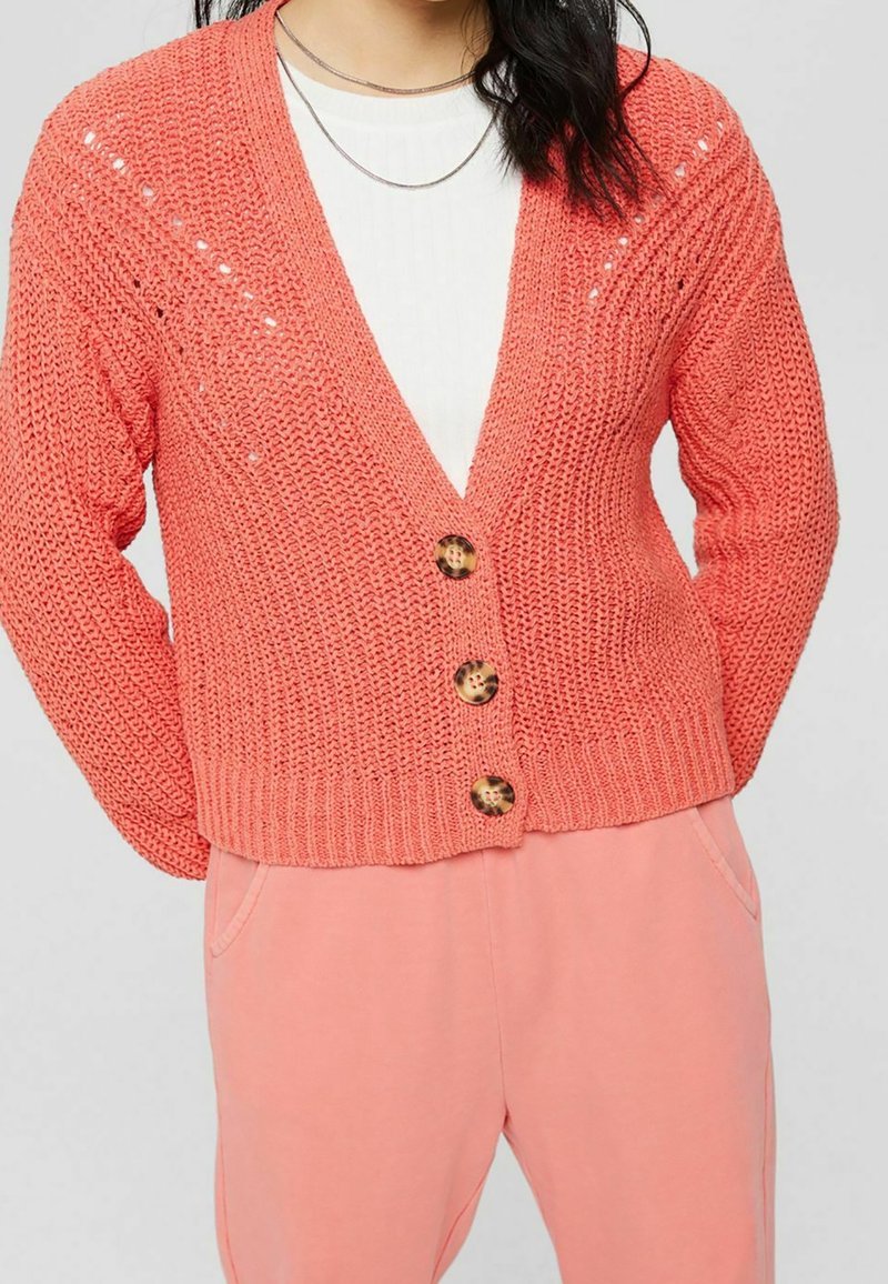 Koraal kleurige gebreide cardigan met een diepe V-hals, drop schouders en drie grote knopen. Bevat een geribbelde zoom en open steekdetails.