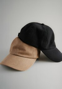 Due cappellini da baseball impilati, uno nero e uno beige. Entrambi realizzati in cotone testurizzato, con visiere curve e un piccolo bottone in cima.