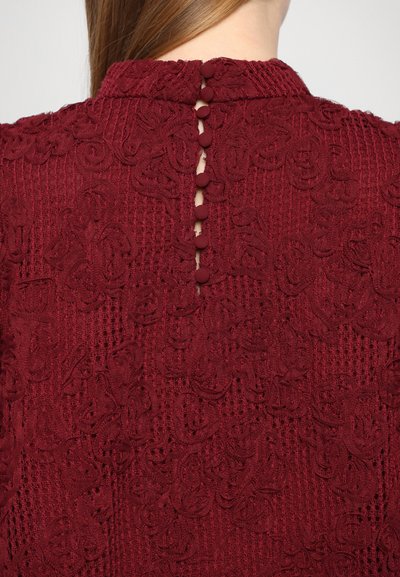 Burgundy top featuring textured floral embroidery, a high neckline, and a keyhole back closure with five fabric-covered buttons.