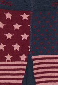 Kniestrümpfe mit einem Patchwork-Design in Rot und Marineblau. Die Muster umfassen Sterne, Pünktchen und Streifen in unterschiedlichen Abschnitten.