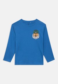 Μπλε μακρυμάνικο πουκάμισο με εκτύπωση μιας τίγρης που φοράει πράσινο σκουφάκι με την ετικέτα "BEAST" στο αριστερό στήθος.