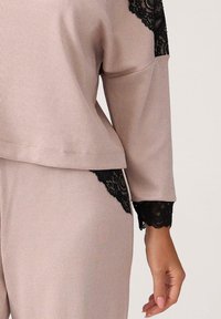 Długi rękaw top w jasnoróżowym prążkowanym materiale, z czarnymi koronkowymi akcentami na ramionach i rękawach, z luźnym krojem na dole.