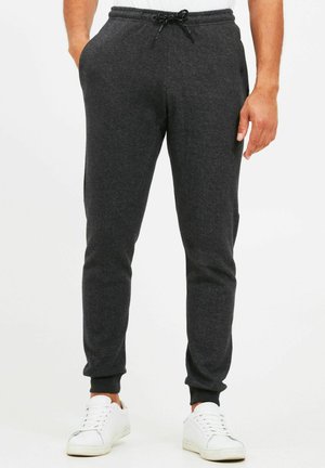 Dark gray sweatpants made from soft fabric, featuring an elastic waistband with drawstring, side pockets, and ribbed cuffs. Worn with white sneakers.